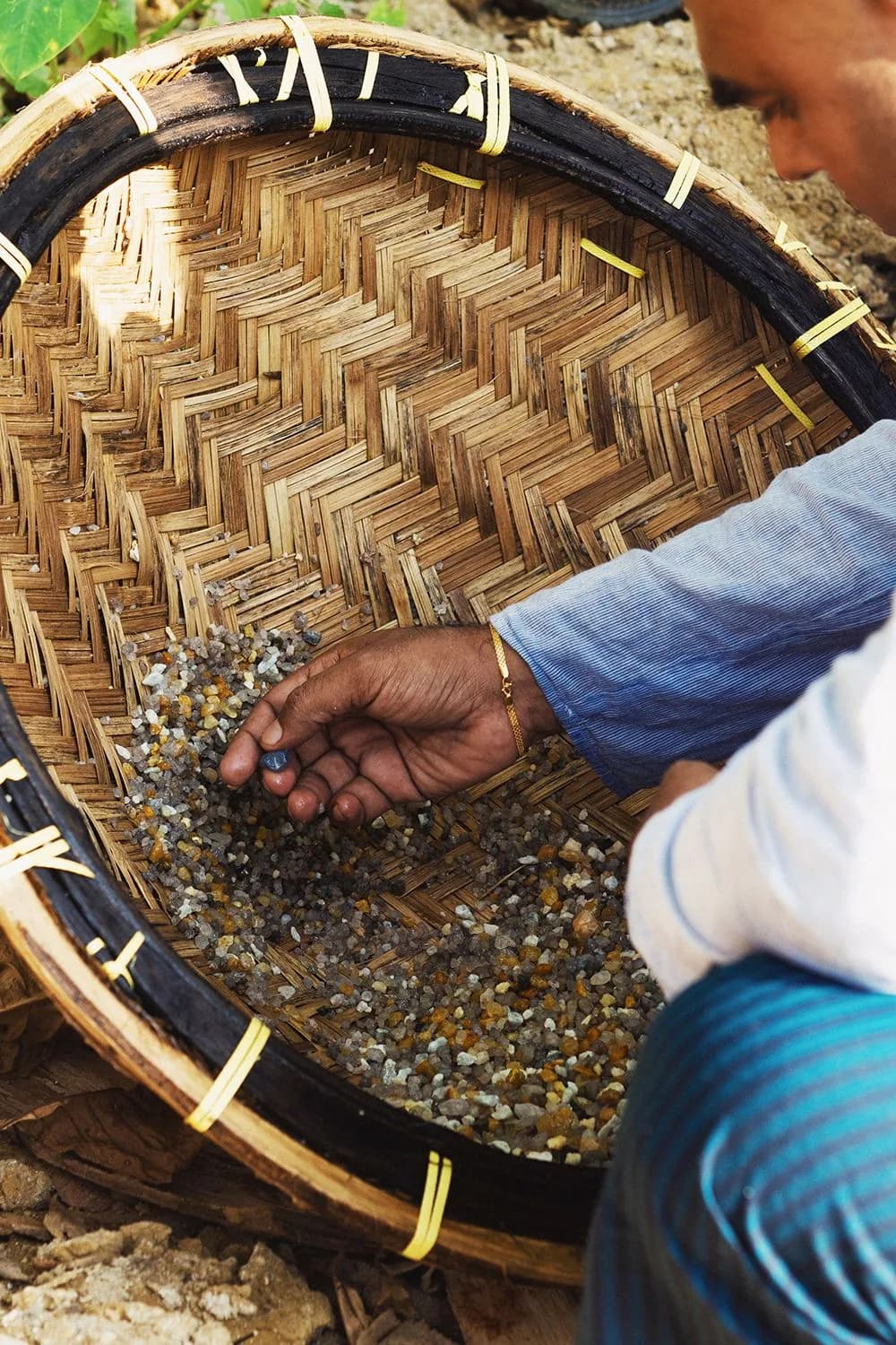 A miner sorting gem-bearing gravel in a woven basket