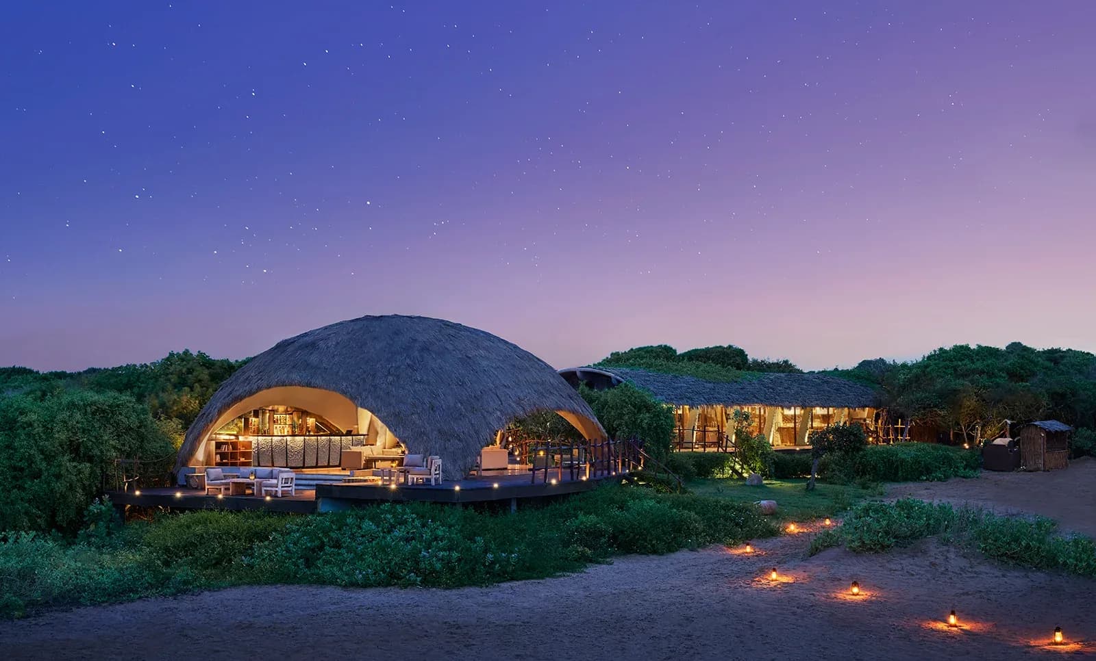 Uga Chena Huts’ illuminated lodge buildings beneath a purple evening sky