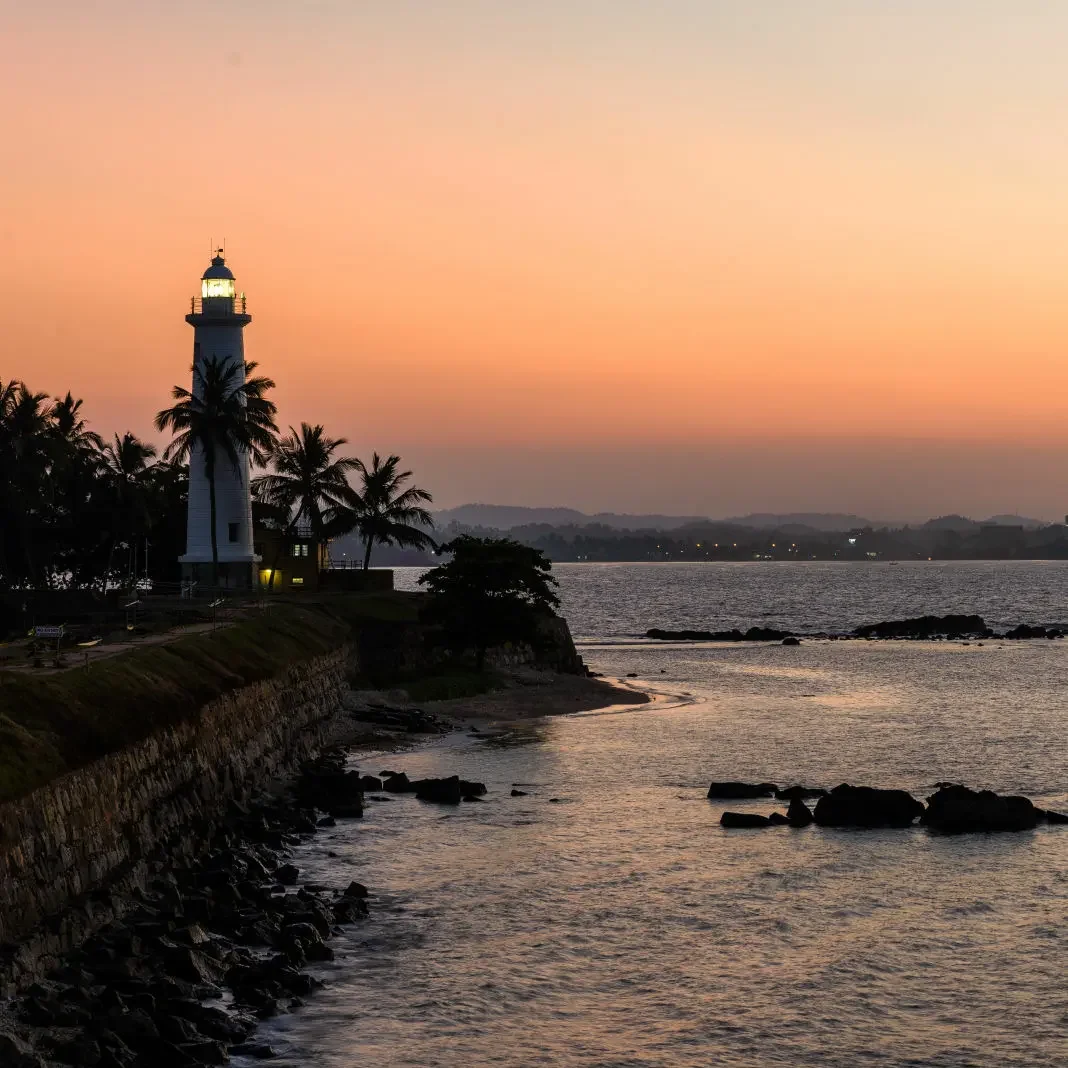 Galle Lighthouse and the fort ramparts beside the Indian Ocean at sunset